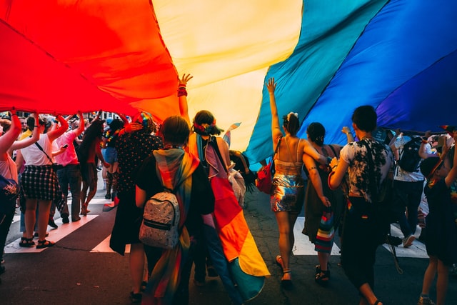 An image of people walking under a rainbow flag
