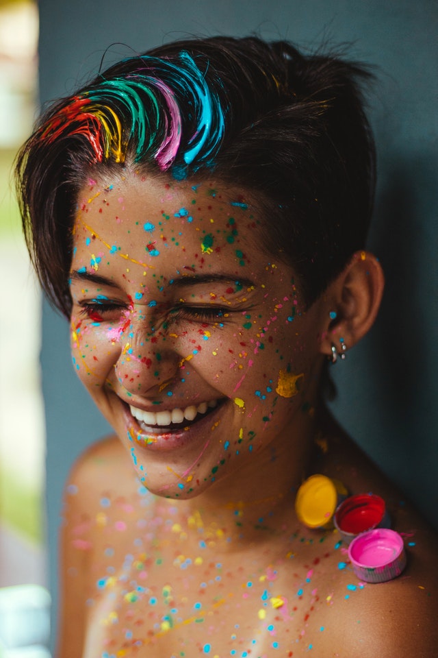 An image of a person with rainbow-coloured confetti on them, as well as rainbouw-coloured stripes in their hair